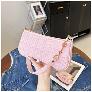 Détail d'un sac bandoulière rose tissé avec breloque fleurie dorée et bandoulière en cuir