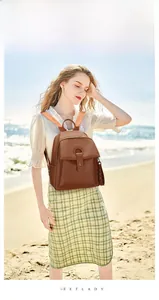 Brown litchi grain leather backpack with buckle pocket detail in sunny outdoor setting