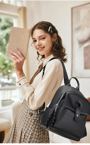 Detail of black pebbled leather backpack showing side pockets and front buckle flap