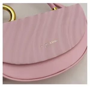 Close-up of pink saddle bag with wavy textured flap and gold metal hardware