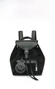 Detail of minimalist black backpack featuring a smiley charm and metallic lock accent
