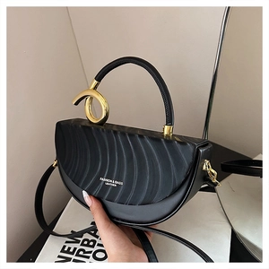 Detail of black semi-circular saddle bag with wavy texture and gold spiral metal handle