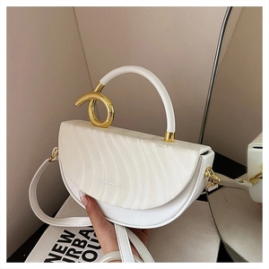 Detail of white saddle bag featuring gold metal knot and wave texture on the flap