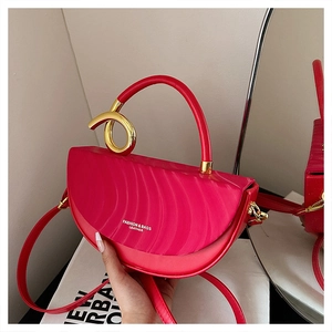 Detail of red crescent leather bag featuring wave textures and a gold twisted handle