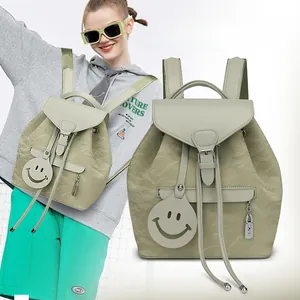 Detail of light green backpack showing pleated texture, drawstring closure, and smiley charm