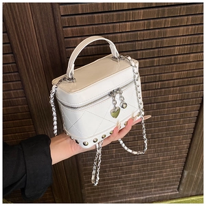 Dettaglio mini borsa bianca trapuntata con catena argento e ciondolo a cuore su legno