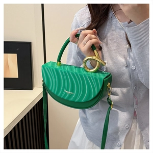 Green saddle bag with wavy texture and gold ring handle held by a model
