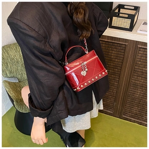 Dettaglio borsa vanity in vernice rossa con rivetti dorati e ciondolo a cuore