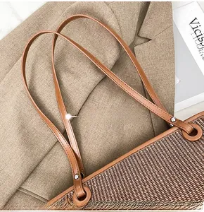 Close-up of woven straw tote bag with leather straps on a brown blazer and magazine
