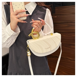 Detail of white half-moon bag featuring textured faux leather and golden ring handle