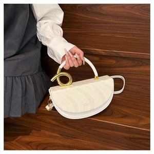 Detailed view of white saddle bag with unique golden twisted metal handle and fine leather strap
