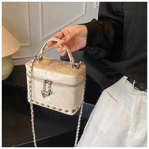 Dettaglio borsa a scatola in vernice beige trapuntata con borchie e ciondolo a cuore