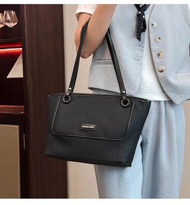 Detail of black woven tote bag with a decorative front pocket and metallic fashion logo