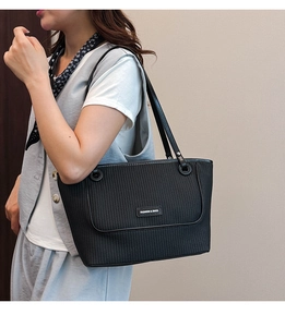 Detail of black pleated tote bag with silver logo plaque worn by a model on shoulder