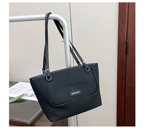 Detail of black tote bag featuring woven texture panel and silver metal buckle connectors