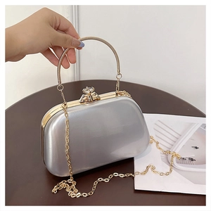 Detail of silver evening clutch featuring a gold circular handle and crystal lock