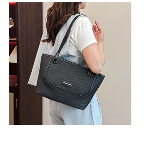 Black woven tote bag detail showing slim leather straps and brand logo plaque on shoulder