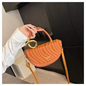 Detail of orange saddle bag with gold knotted handle and wave-embossed leather texture