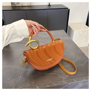 Close-up of caramel saddle bag featuring wave pattern detail and gold metal handle