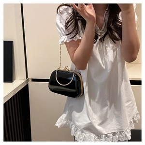 Close-up of black patent leather evening bag with gold chain and ring handle on white dress