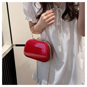 Close-up of a red glossy evening clutch with a round gold handle and metal chain strap