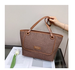 Close-up of brown woven straw tote bag with synthetic leather handles and fashion logo