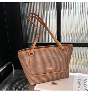 Detail of woven straw tote bag with brown leather handles and fashion logo plate