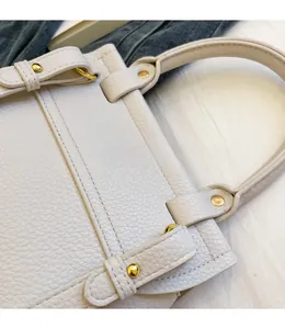 Dettaglio di borsa a mano bianca in pelle martellata con rivetti dorati e cuciture