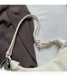Detail of a creamy white pleated shoulder bag with knotted strap and silver hardware accents