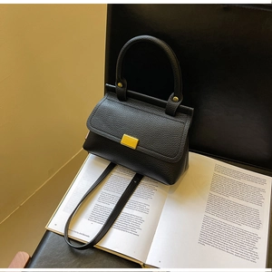 Dettaglio borsa a mano in pelle martellata nera con fibbia dorata su libro