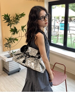 Detail of silver sequined tote bag with black leather trim shown in a modern cafe setting