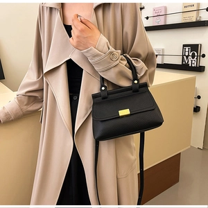 Dettaglio borsa nera in pelle a grana con fibbia dorata indossata con un trench coat