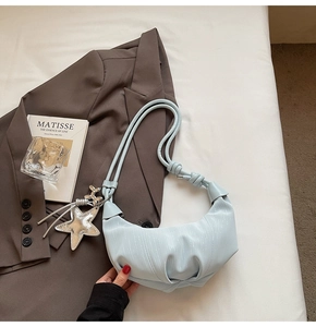Detail of light blue pleated croissant bag with silver star charm on a chic background