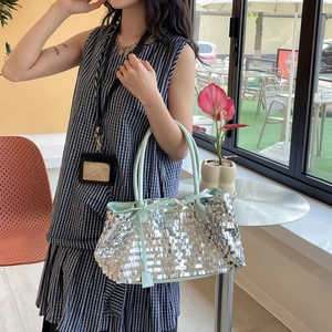 Detail of silver sequin tote bag with light green leather straps in a cafe setting