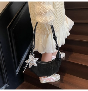Detail of a black pleated hobo bag with a silver star charm on a wooden staircase