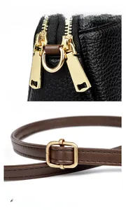 Detailed view of dual golden zippers and adjustable brown leather strap on black handbag
