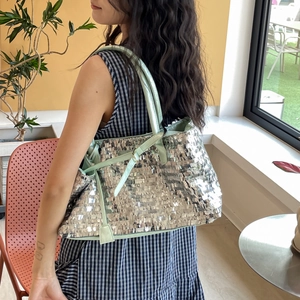 Detail of silver sequin tote bag with light green straps on model in bright room