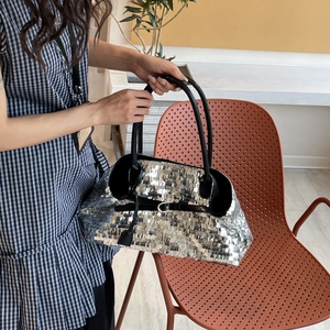 Detailed close-up of a silver sequin tote bag with black leather straps and metal buckle