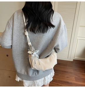 Close-up of a cream pleated hobo bag with a silver star charm on a model shoulder