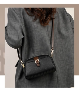 Detail of black pebbled leather crossbody bag featuring brown strap and gold metal hardware