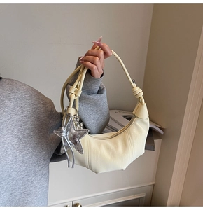 Detail of light beige pleated crescent bag with a silver star pendant and knotted strap