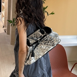 Detailed view of silver sequin tote bag with black leather straps worn by model