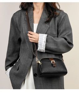 Detail of black pebbled leather crossbody bag with brown strap on grey blazer