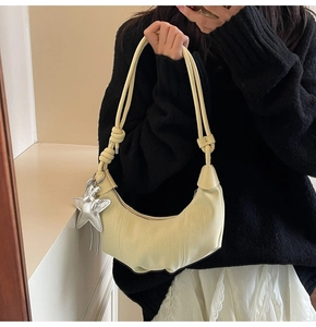 Detail of a pleated crescent shoulder bag in cream with a silver star pendant and knot strap