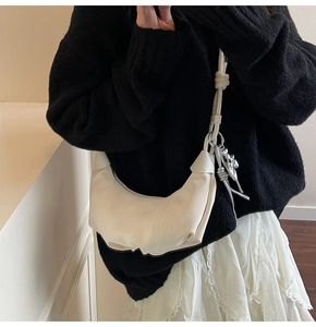 Detail of off-white pleated dumpling bag with silver flower charm and soft faux leather texture