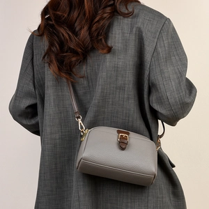 Detail of grey lychee leather crossbody bag with brown straps on a grey blazer suit