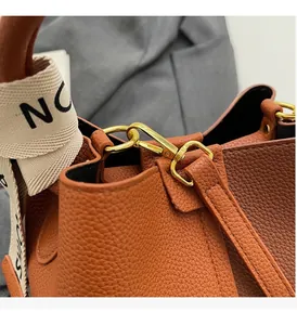 Detail of golden metal hook and litchi grain leather texture on the brown bucket bag