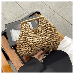 Close-up of hand-woven straw handbag with elegant gold chain strap on a wooden bench