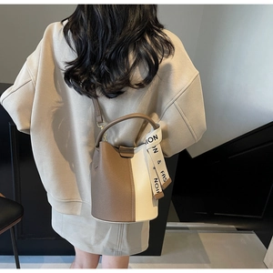 Crossbody view of a two-tone lychee textured bucket bag with decorative fashion strap
