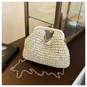 Close-up of beige woven straw handbag with a rigid handle and gold metal chain strap
